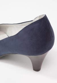 Chaussure femme en daim bleu marine à petit talon, bout arrondi et talon empilé gris clair sur fond blanc.