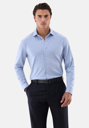 Helles blaues Langarmhemd mit Button-down-Kragen, taillierter Passform und weißen Knöpfen, getragen mit dunklen Hosen und einem schwarzen Gürtel.