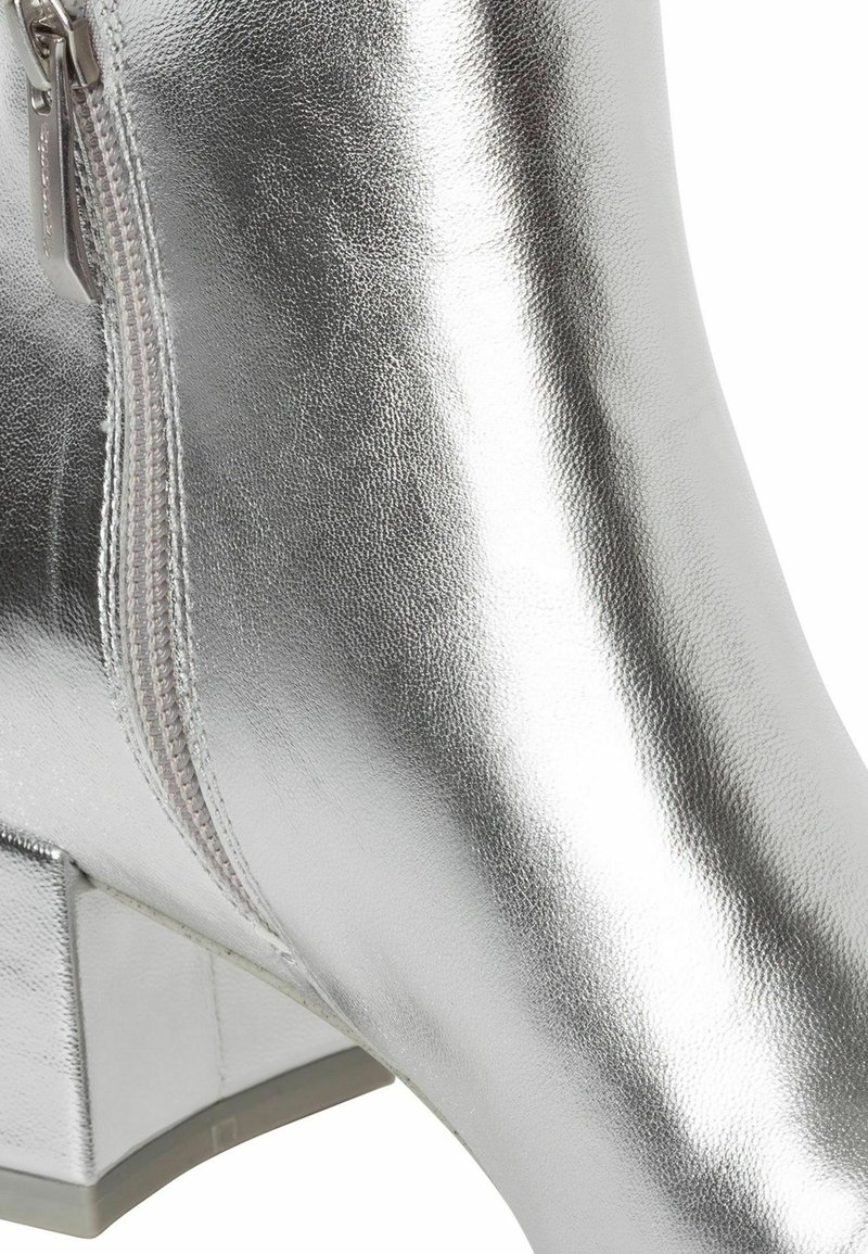 Close-up van een glanzende zilveren enkelboot met blokhak en zichtbare zijrits.