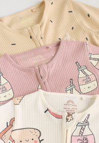 Three baby tops: pink with milk carton print, cream with toast design, and beige with seed pattern; ribbed cotton texture, button closures.