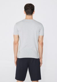 Camiseta de algodón gris con mangas cortas, diseño ajustado y espalda lisa, combinada con pantalones cortos oscuros, que muestra la textura del tejido y la simplicidad.