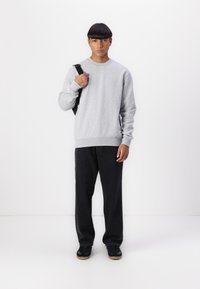Hanorac gri cu mâneci lungi și tiv resirat, purtat cu pantaloni largi negri. Sneakers negri completează ținuta.