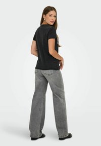 Zwarte T-shirt met korte mouwen en een ronde hals, gecombineerd met wijdvallende grijze jeans. De outfit heeft minimale details en een relaxte pasvorm.