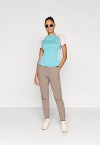 Αθλητική μπλούζα σε ανοιχτό γαλάζιο και ροζ χρώμα με εφαρμοστή σχεδίαση, συνδυασμένη με μπεζ παντελόνι στενής γραμμής και ανοιχτόχρωμα αθλητικά παπούτσια. Περιλαμβάνονται γυαλιά ηλίου.