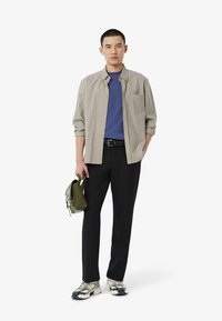 Beige ja ruskea ruutupaita sinisen T-paidan päällä, yhdistettynä mustiin housuihin ja maastokuvioisiin lenkkareihin. Vihreä olkalaukku kädessä.