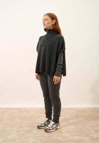 Poncho in lana grigia con colletto alto, abbinato a pantaloni aderenti coordinati e sneakers grigie con accenti neri e bianchi.