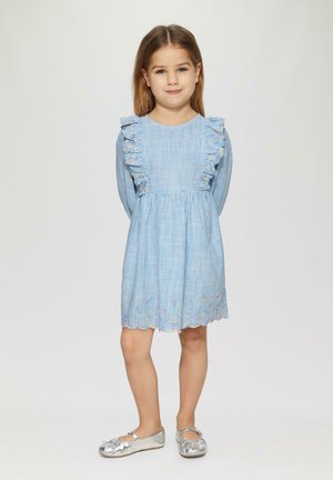 Blau gestreiftes Kleid mit Rüschenschultern, floralem Stickmotiv am Saum und gewelltem Rand. Kombiniert mit silbernen Ballettschuhen.