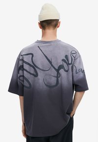 Camiseta gris degradada de manga corta con letras abstractas negras en la parte posterior; hecha de algodón suave con un ajuste relajado.