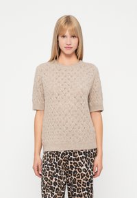 Κοντομάνικο κρεμ πλεκτό πουλόβερ με υφή σε διαμαντένιο μοτίβο, συνδυασμένο με παντελόνι λεοπάρ με καφέ και μαύρες αποχρώσεις.