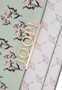 Grön och vit mönstrad plånbok med blommönster och en guldig logotypaccent. Konstruerad av strukturerad konstläder.