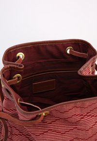 Rød mønstret stof spandtaske med brune læderdetaljer og guldnitter. Indersiden viser et dybt rum med en læderetiket.