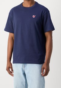 Marineblå bomulds-T-shirt med rund hals, korte ærmer og et lille rødt logo på venstre bryst. Har en afslappet pasform.