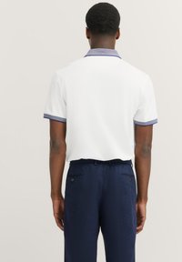 Witte polo met korte mouwen, met een marineblauwe kraag en manchetten. De achterkant toont gladde stof en een ontspannen pasvorm.