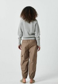 Ljust grå ribbad tröja med elastisk fåll, kombinerad med avslappnade bruna cargobyxor med sidofickor och elastiska muddar.