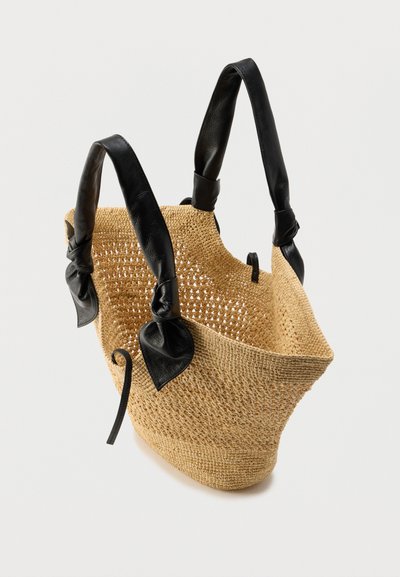 Πλεκτή τσάντα ώμου από ψάθα με μαύρες δερμάτινες χειρολαβές, που διαθέτει στρογγυλεμένο σχήμα, ανοιχτό πάνω μέρος και διακοσμητικές κόμπους στις χειρολαβές.