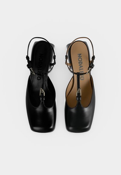 Ζεύγος μαύρα δερμάτινα παπούτσια slingback με τετράγωνες μύτες και λεπτά λουράκια στον αστράγαλο, το ένα με μαύρη και το άλλο με ταμπά εσωτερική σόλα, από πάνω.