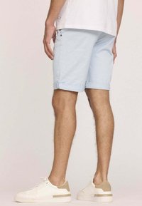 Shorts en coton bleu clair avec des revers, poches latérales, et une texture lisse, assortis à des baskets blanches avec des accents beiges.