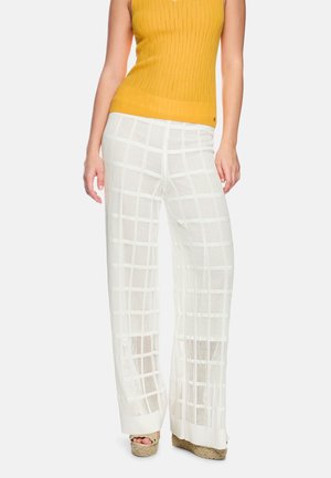 Woman wearing white wide-leg mesh pants with a grid pattern, yellow sleeveless ribbed top, and beige wedge sandals.