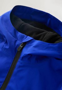 Blue jacket with a soft black fleece lining, featuring a front zipper and a structured collar, made from smooth, waterproof material.