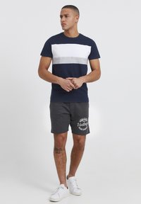T-shirt navy avec des rayures horizontales blanches et grises, associé à un short gris foncé avec un imprimé graphique blanc. Baskets blanches.