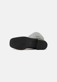 Grijze leren enkellaars met een ronde neus, gestructureerd oppervlak en een zwarte rubberen loopzool met een horizontaal geribbeld patroon voor grip.