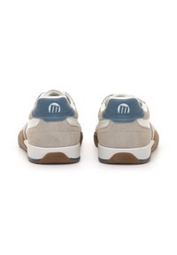 Par de zapatillas deportivas informales en beige y blanco con detalles azules en el talón y suelas marrones, mostradas desde atrás sobre un fondo blanco.