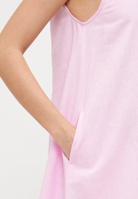 Vestido de lino rosa con un diseño sin mangas y un bolsillo lateral. La tela tiene un acabado ligeramente texturizado.