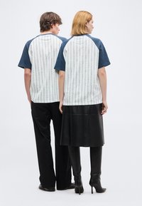 Δύο άτομα που κοιτάζουν προς τα πίσω, φορούν ταιριαστές λευκές και ναυτικές κοντομάνικες μπλούζες με κάθετα σχέδια, συνδυασμένες με μαύρο παντελόνι και μπότες.