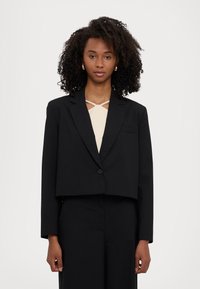 Blazer noir court en tissu lisse, avec une fermeture à un bouton, des revers crantés et une poche avant sur le côté gauche.