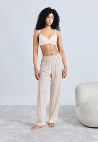 Reggiseno leggero beige con scollo a V e spalline regolabili abbinato a pantaloni da pigiama larghi a righe di colore crema. Tessuto morbido e vestibilità rilassata.