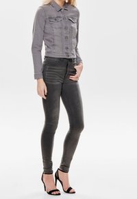 Chaqueta de mezclilla gris y jeans ajustados grises con un diseño entallado. Cuello afilado, bolsillos frontales y tacones altos negros con tiras.