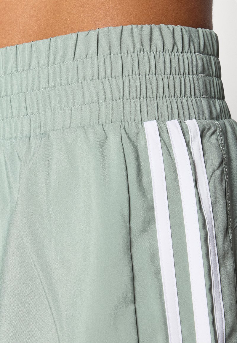 Shorts vert clair avec une taille élastique, dotés de rayures latérales blanches et d'une texture de tissu lisse et léger.