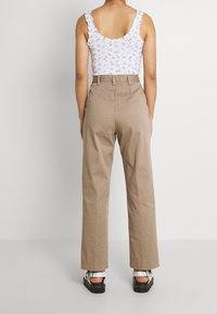 Vit blommönstrad linne med volangaxlar, kombinerad med högmidjade, beiga byxor med vida ben och svarta plattformssandaler.