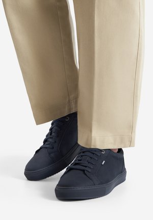 Zapatilla deportiva azul marino con textura lisa, puntera redonda y perfil bajo. Presenta cordones, ojales reforzados y una suela de goma texturizada.