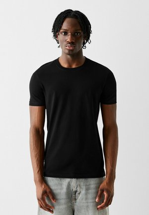 Schwarzes kurzärmliges T-Shirt aus glattem Baumwollstoff mit klassischem Rundhalsausschnitt, kombiniert mit hellen Jeans.