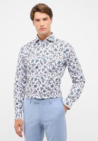Wit shirt met een blauw en bruin bloemmotief, met een button-down kraag en lange mouwen, gecombineerd met lichtblauwe broeken.