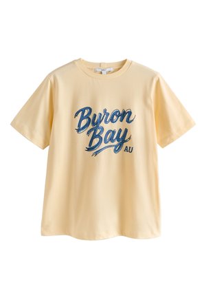 Hellgelbes T-Shirt mit kurzen Ärmeln und großem blauen Schriftzug "Byron Bay AU" auf der Vorderseite.