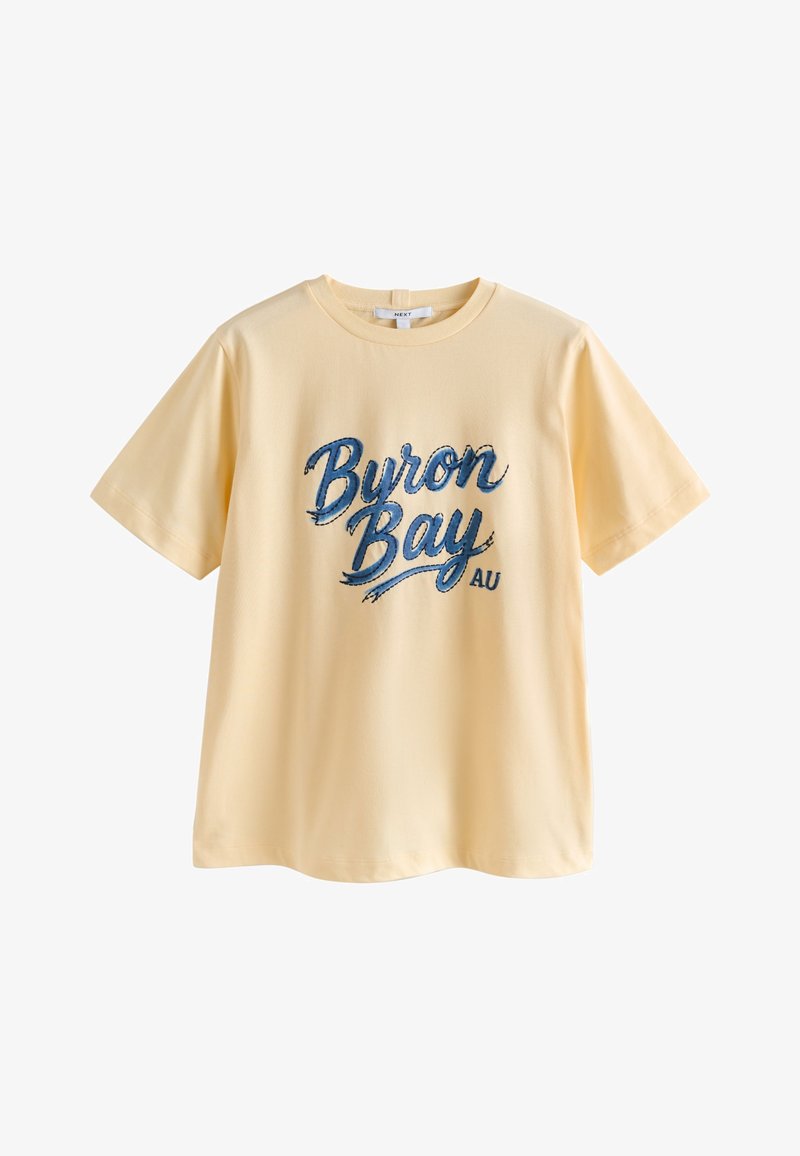 T-shirt jaune clair à manches courtes avec « Byron Bay AU » en grand texte manuscrit bleu à l'avant.