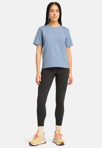 Lyseblå bomulds t-shirt med korte ærmer og rund halsudskæring, parret med sorte leggings og multifarvede sportsko.