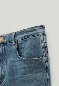 Vaaleansiniset farkut, joissa on klassinen viiden taskun muotoilu, hopeiset nappikoristeet ja hieman haalistunut pinta.