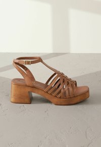 Bruine leren plateau-sandaal met een geweven ontwerp, open tenen, verstelbare enkelband en een blokhak, met een natuurlijke houtafwerking.
