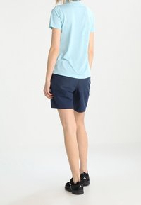 Světle modrá košile s krátkým rukávem a tmavě modré šortky, doplněné černými teniskami. Šortky mají texturovaný design, což vytváří neformální vzhled.