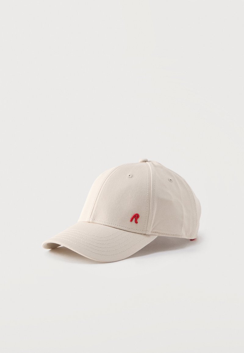 Casquette de baseball beige avec visière courbée, trous de ventilation et petit "R" rouge brodé sur le panneau avant, présentée sur un fond blanc.