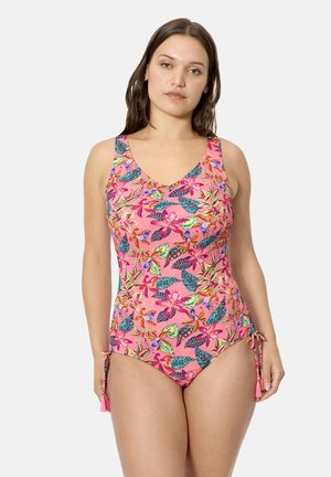 Mujer con un traje de baño rosa de una pieza con patrones florales y de hojas multicolores, con lazos ajustables en las caderas.