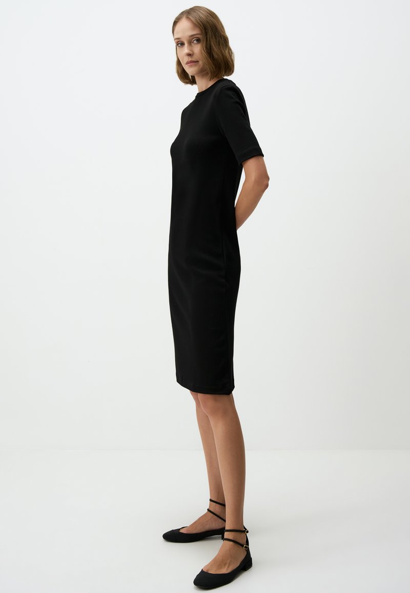 Robe noire ajustée à manches courtes et encolure ronde. Texture lisse, design longueur genou, assortie à des ballerines noires avec des brides autour de la cheville.