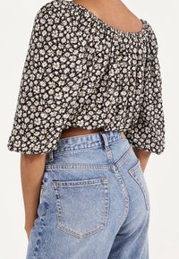 Crop top floreale nero con maniche a sbuffo, decorato con piccole margherite bianche e accenti gialli. Abbinato a jeans azzurri a vita alta.