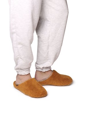 Brune, fuzzy hjemmesko lavet af blødt materiale, med en rund form, åben bag og dekorativ syning langs kanten.