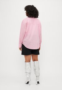 Ροζ ριγέ πουκάμισο με μακριά μανίκια, καμπύλη άκρη, συνδυασμένο με μαύρες βερμούδες και γυαλιστερά ασημένια μπότες μέχρι το γόνατο.