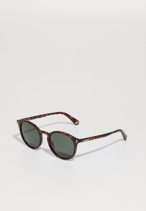 Óculos de sol tortoise circular com lentes escuras. Logótipo Polaroid na haste e um detalhe em arco-íris na parte do braço. Textura suave.