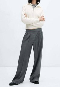 Un pull zippé en maille côtelée blanche associé à un pantalon gris taille haute, ample, avec des plis et une texture lisse.